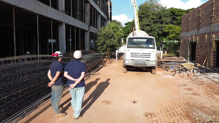 Dois profissionais de capacete em uma obra, com caminhão da CONCRECIA ao fundo